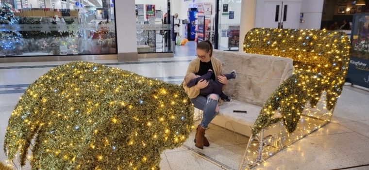 Jessica breastfeeding her 15 month old child, sitting in a sleigh while doing their Christmas shopping.