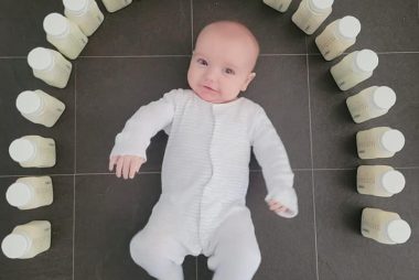 A baby is lying on the floor surrounded by bottles of expressed milk